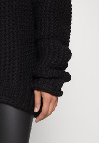 Schwarzer Strickpullover mit einer strukturierten, groben Optik. Mit umgeschlagenen Bündchen und einem gerippten Saum, kombiniert mit eleganten schwarzen Leggings.