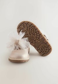 Hellrosa metallische Schuhe mit einer durchsichtigen weißen Tüllschleife. Braune Gummisohle mit einem floralen Muster. Rundes Zehendesign, Knöchelhöhe.