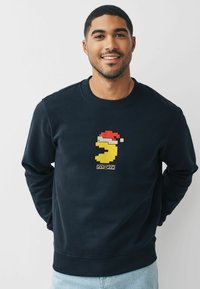 Felpa blu navy con logo di Pac-Man pixelato e cappello di Babbo Natale rosso sul petto. Tessuto morbido con polsini e orlo ribattuti.