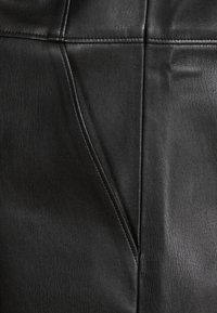 Cuero negro con una textura suave, que presenta costuras cosidas y un diseño de panel vertical. La superficie muestra un ligero brillo y flexibilidad.