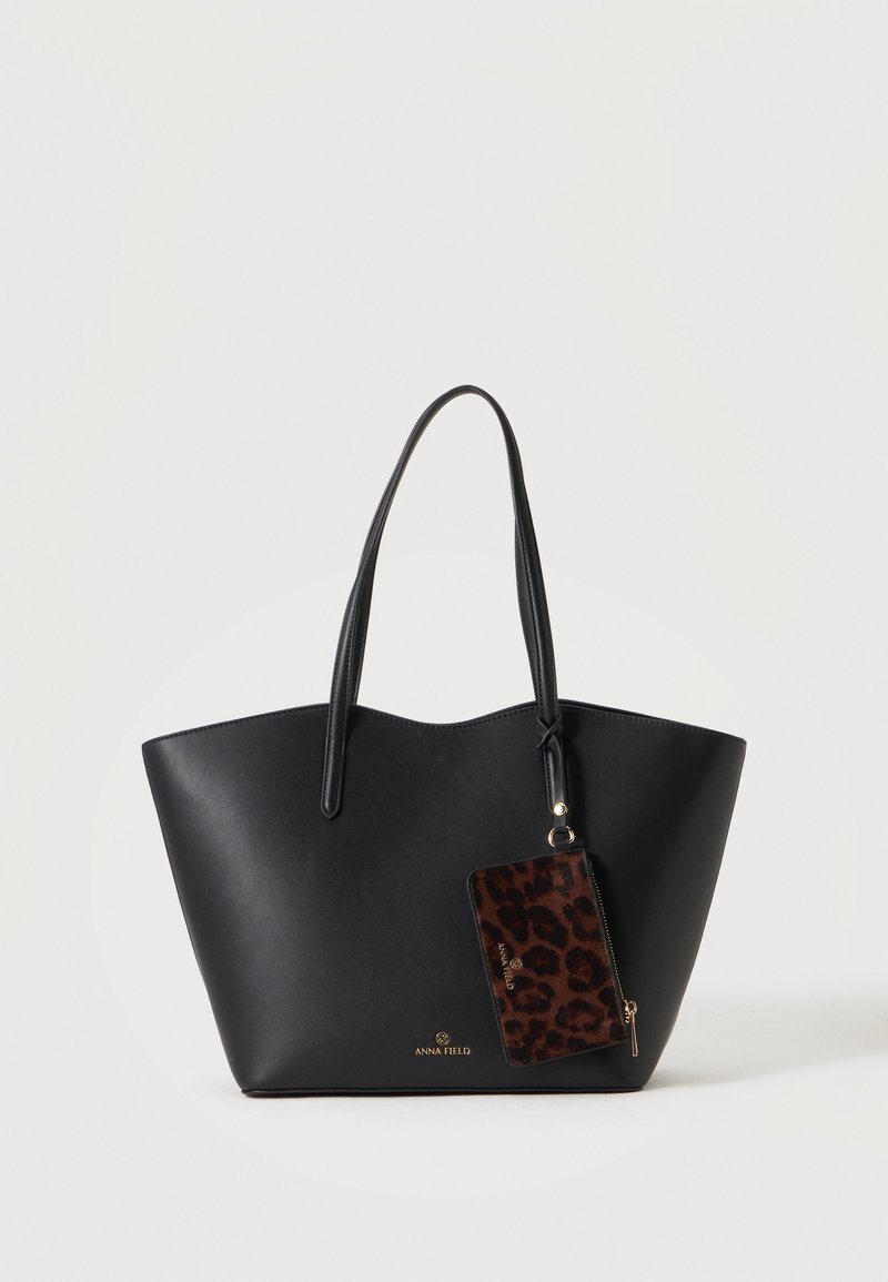 Sac fourre-tout noir avec deux poignées et une pochette léopard attachée, présenté sur un fond clair uni.