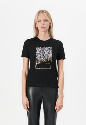 T-shirt noire avec un graphique imprimé léopard et des accents dorés, à manches courtes et à coupe décontractée. Porté avec un pantalon en cuir noir.