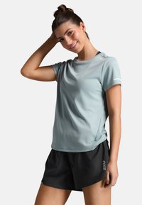 Světle modré sportovní tričko s krátkým rukávem a kulatým výstřihem, kombinované s černými šortkami s bočním logem. Hladká, vlhkost odvádějící tkanina.