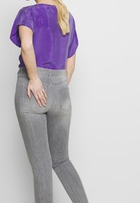 Lila topp med korta ärmar tillsammans med gråa, figurnära jeans. Jeansen har en blekt textur med bakfickor och en midjehög midjeresår.