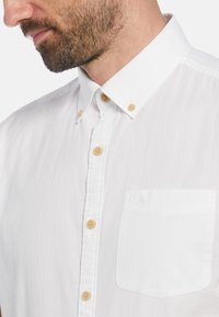 Witte button-up shirt met een textuurstof, klassieke kraag, beige knopen en een subtiele geborduurde logo op de borstzak.