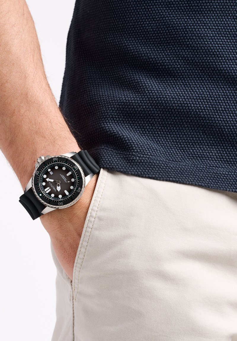 Potapljaško uro z črnim gumijastim trakcem, srebrnim nerjavnim jeklenim ohišjem, črnim številčnico, sijočimi oznakami in vrtljivim okvirjem, ki je nosi na zapestju.