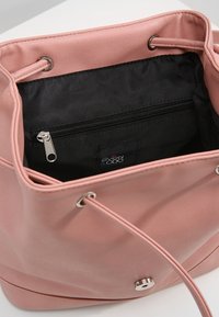 Rosa dragsäck med snörning som visar ett öppet inre med en svart dragkedjeficka och silverfärgade metallaccenter.