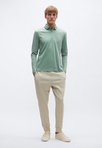 Világoszöld, hosszú ujjú galléros póló, bézs, szabott nadrággal, amely szűkített szárú és bordázott mandzsettával rendelkezik. Klasszikus sportcipővel egészül ki a megjelenés.