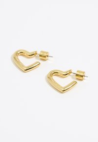 Boucles d'oreilles en métal doré avec une forme de crochet courbé, présentant une surface lisse et brillante et un dos cylindrique pour un maintien sécurisé.