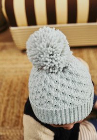 Beanie tricoté bleu clair avec un motif texturé et un pompon duveteux sur le dessus. Présente un poignet côtelé pour un ajustement serré.