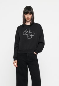 Zwarte sweatshirt met een ronde hals, losse pasvorm en lange mouwen. Bevat een gestructureerd logo in metallic zilver op de voorkant.