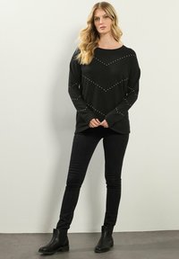 Pullover nero a maniche lunghe con un motivo a zig zag realizzato con dettagli di borchie, abbinato a jeans neri aderenti e stivali alla caviglia.