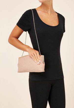 Bolso de mano rosa con textura suave, correa de cadena plateada y cierre superior metálico, sostenido en la mano contra una blusa negra.