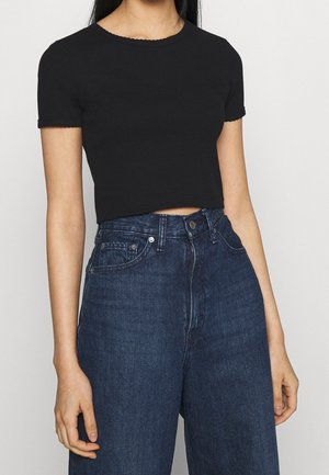 Czarna krótka koszulka z krótkim rękawem, o żebrowanej teksturze i falbaniastym dekolcie, zestawiona z dżinsami o wysokim stanie w ciemnym kolorze.