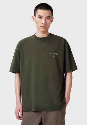 Olijfgroene katoenen T-shirt met een ronde hals, korte mouwen en een klein wit logo op de linkerborst. Relaxte pasvorm en een eentonige kleur.