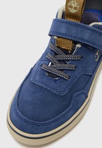 Baskets en daim bleu avec une surface texturée, languette rembourrée et sangle marron. Présente des couleurs de lacets contrastantes et une fine semelle en caoutchouc.