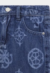 Denim jeans hebben een donkerblauwe wassing met subtiele, gegraveerde patronen en hardwaredetails, inclusief een metalen knoop en een voorzak.