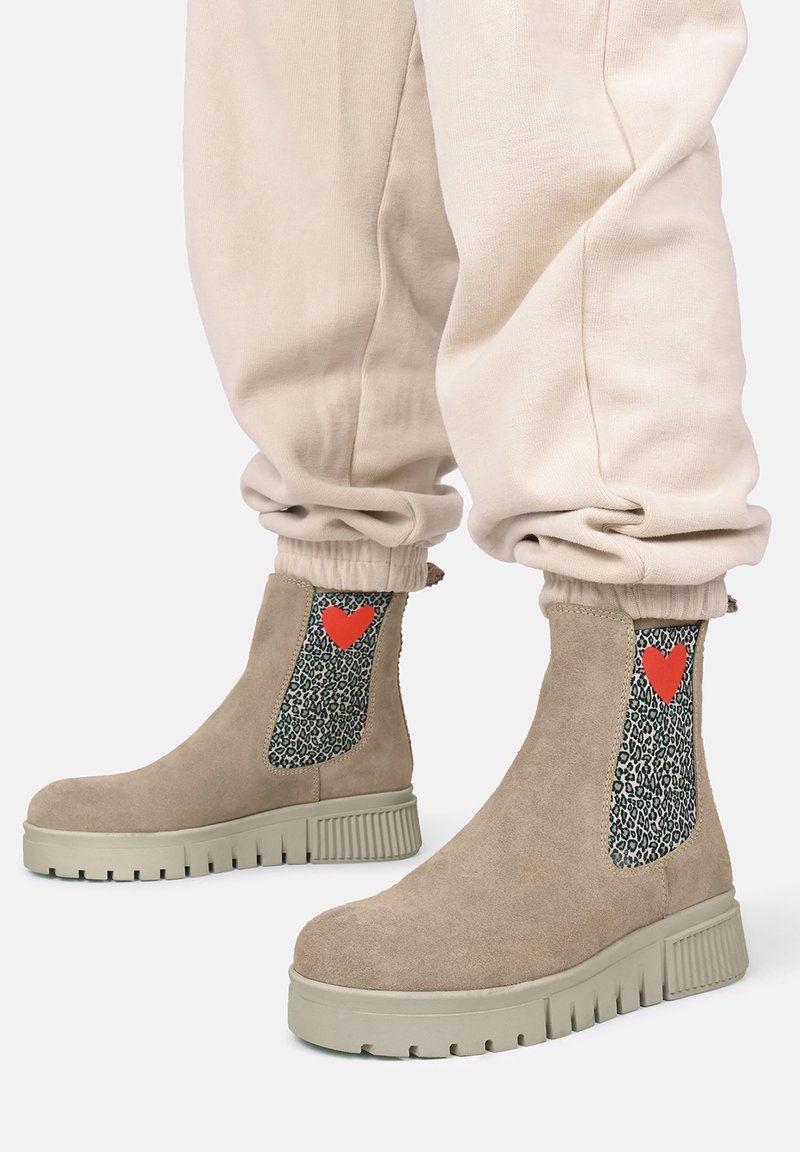 Beżowe zamszowe botki za kostkę z masywną szaro-skalową podeszwą, z panelami w leopardzi wzór po bokach i czerwoną serduszkiem na każdej bucie.