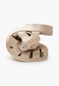 Beige molded shoe with cutouts and a transparent buckle. Textured surface with a smooth finish. Low profile design for comfort.
