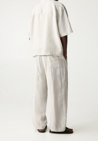 Vaaleanbeige lyhythihainen pellavapaita, joka on yhdistetty samansävyisiin leveälahkeisiin pellavahousuihin, joissa on sivutaskut ja rento mitoitus.