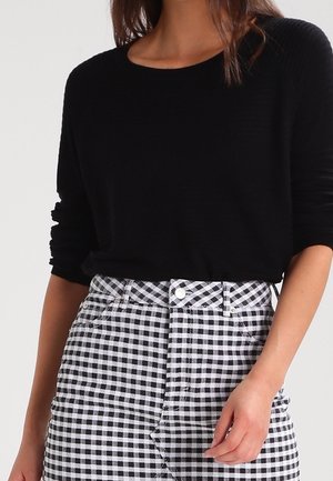 Maglione nero a coste con scollatura rotonda, abbinato a una gonna a quadri bianca e nera con vita alta e bottoni frontali.