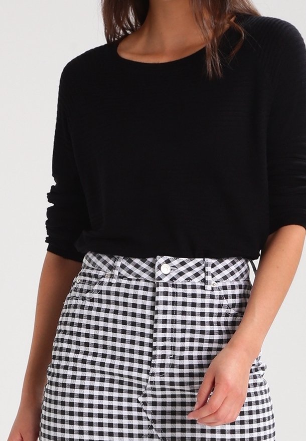 Maglione nero a coste con scollatura rotonda, abbinato a una gonna a quadri bianca e nera con vita alta e bottoni frontali.