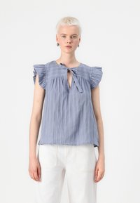 Bluză albastră cu dungi, cu mâneci scurte cu volane, decolteu în formă de lacrimă și detaliu cu fundiță. Fabricată dintr-un material ușor, cu textură fină.