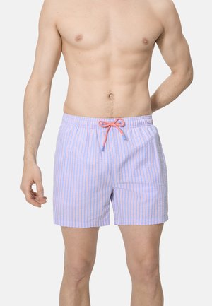 Hombre sin camisa con pantalones de baño azul claro con rayas verticales rosas y blancas y un cordón rosa atado en un lazo en la cintura.