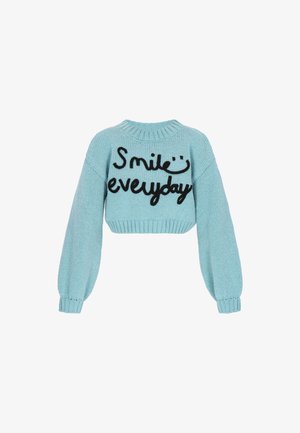 Helleblaue gestrickte kurze Sweater mit langen Ärmeln und schwarzem Text "Lächle jeden Tag" mit einem Smiley über dem Text.