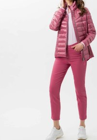Chaqueta acolchada rosa con un cuello alto, combinada con pantalones rosa ajustados y zapatillas blancas. La chaqueta tiene cremallera y textura acolchada.