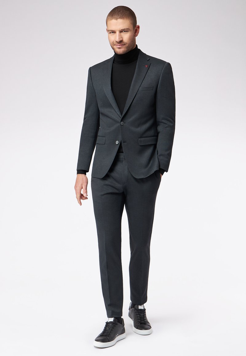 Ciemnoszary garnitur o slim fit, jednorzędowa marynarka, kontrastowy czarny golf oraz czarne sneakersy z białymi podeszwami. Minimalistyczne elementy wzornictwa.