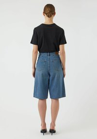 Vaaleansiniset korkeavyötäröiset farkkushortsit, joissa on rento leikkaus, kaksi takataskua ja ruskea nahkainen merkkilappu vyötärön lähellä.