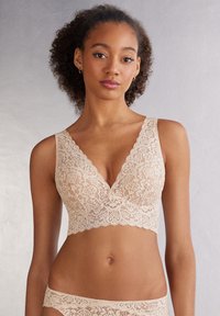 Beige blonde bralette med V-halsudskæring, bølgede kanter og blomsterprint. Blød tekstur, bredere stropper og design uden bøjler for ekstra komfort.