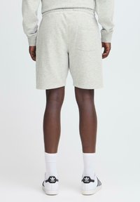 Bermudas de algodón gris claro con un ajuste relajado, cinturilla elástica y un bolsillo trasero único, combinadas con calcetines blancos y zapatos con detalles en negro.