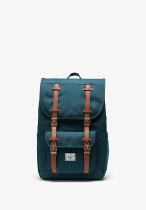 Teal canvas rugzak met bruine leren riemen en hardware, met een voorzak en een logo label aan de onderkant van de voorkant.