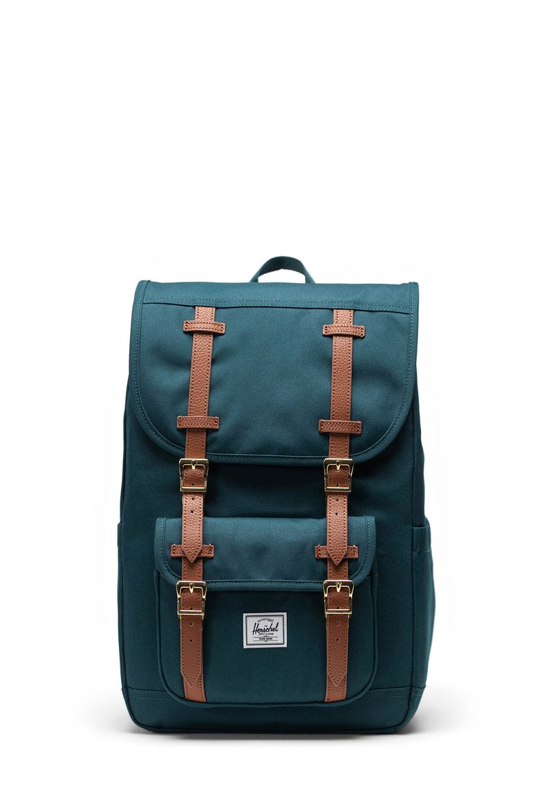 Turargrön canvasryggsäck med bruna läderremmar och detaljer, med en framficka och en logolapp på den nedre framsidan.