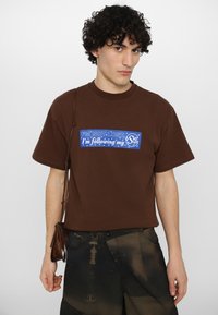 Brown cotton t-shirt with short sleeves, featuring a blue graphic text box that reads "I'M NOT LOST; I'm following my Star Sign."