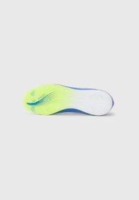 Sole of a blue and yellow soccer cleat featuring molded studs for traction and "MESSI" branding. Background is plain white.