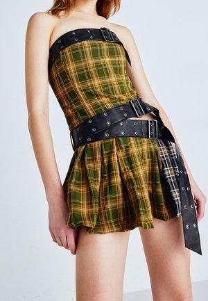 Robe sans bretelles à carreaux verts et jaunes avec des plis superposés, complétée par une ceinture en cuir noir avec des accessoires en métal et des boucles.