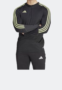 Black athletic top with long sleeves, featuring neon yellow stripes and a half-zip collar. Material appears smooth and fitted.