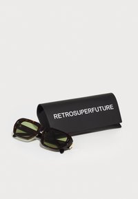 Tortoiseshell prillid roheliste läätsedega, millel on tugeva ristküliku kuju ja kuldsed aktsendid, mustal karbil, millel on kiri "RETROSUPERFUTURE".