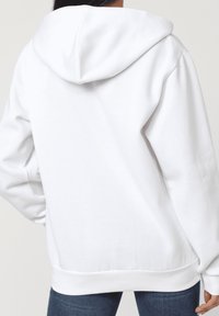 Sudadera blanca con capucha, mangas largas y puños acanalados. Tejido suave con un corte relajado, costuras visibles y una cintura ancha en la parte inferior.
