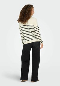 Gestreepte gebreide trui in crème en marineblauw, gecombineerd met brede zwarte jeans. De trui heeft lange mouwen en een ontspannen pasvorm.