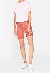 Pantalones cortos de denim rosa con puños doblados, combinados con una camiseta gris clara. El atuendo se complementa con zapatillas blancas. Diseño simple y casual.