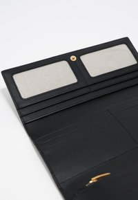 Interior de una billetera de cuero negro con dos ranuras transparentes para tarjetas, múltiples ranuras para tarjetas debajo y un cierre de botón de presión de color dorado.