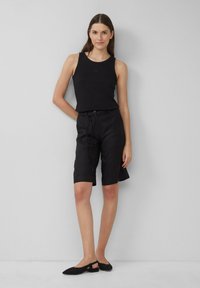 Schwarzes ärmelloses Tanktop, schwarze Leinen-Shorts mit Kordelzug und schwarze Ballerinas. Einfaches Design, lässiger Stil und weiche Texturen.