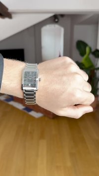 Hõbedane metallist käekell, millel on ristkülikukujuline korpus, musta mustriga kellaplaat, Rooma numbrid ja metallist lingi rihm, kantud käe peal.