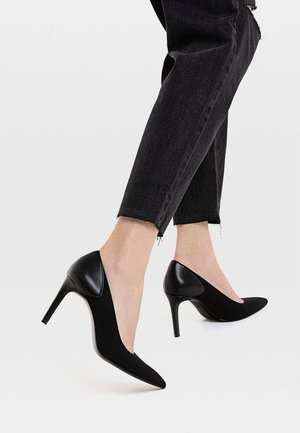 Sorte højhælede sko med spids tå, der har en glat læderbagside og mat stoffront, båret med cropped sorte jeans.