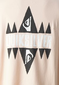 Light beige t-shirt featuring bold black and white Quiksilver logo with triangular shapes and cracked texture in the lettering.