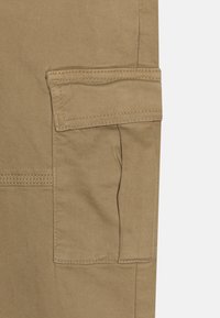 Beige cargobyxor med en sidficka, tillverkade av slitstarkt tyg med synliga sömnadsdetaljer och en mjuk textur.